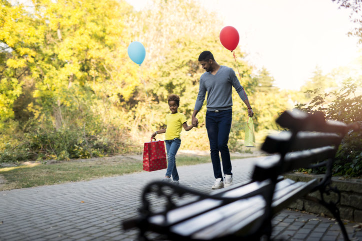 Father and daughter walking in the park after shopping holding hands together.