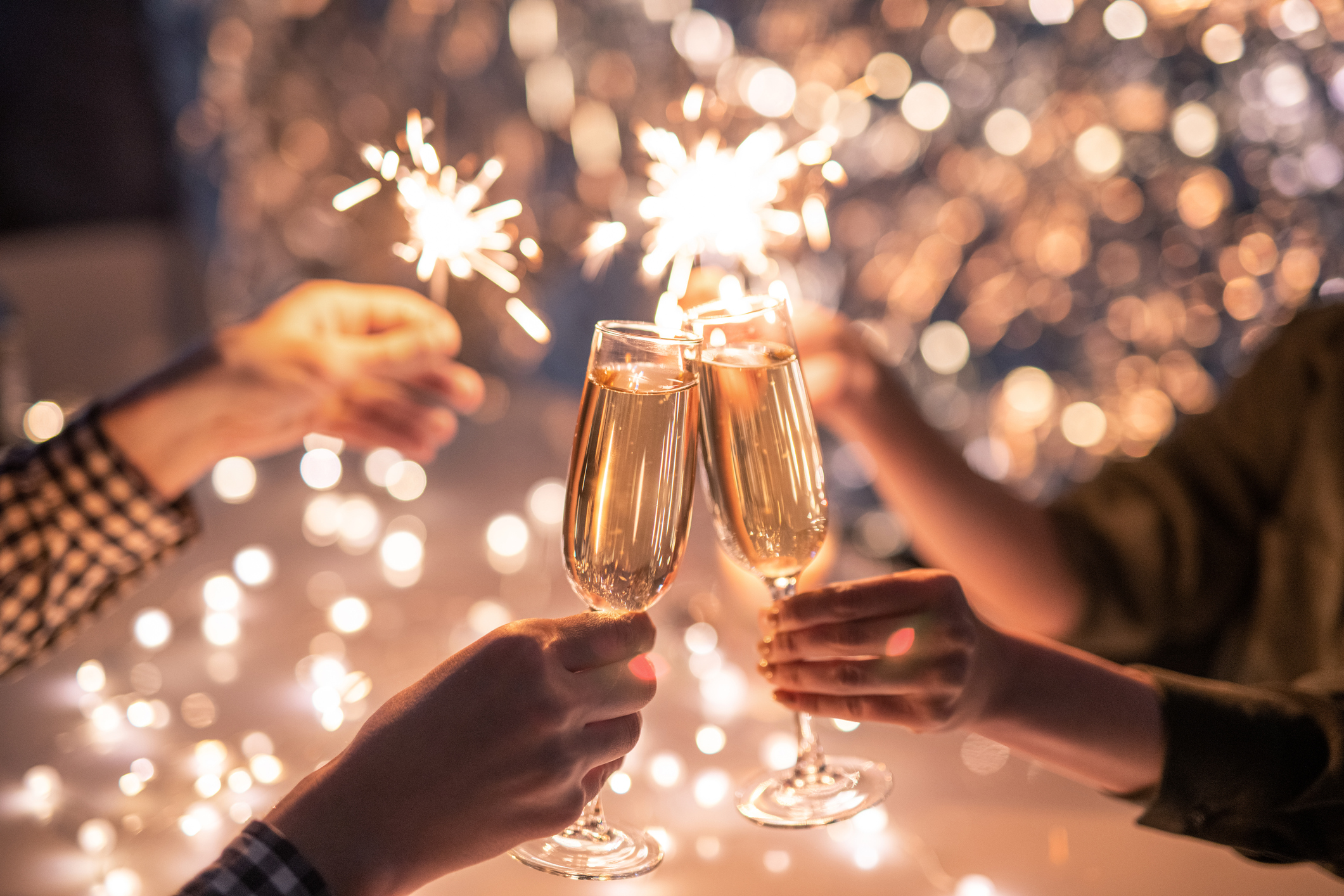 Hands of couple with flutes of champagne and their friends with bengal lights