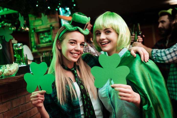 Two girls in a wig and a cap are photographed in a bar.